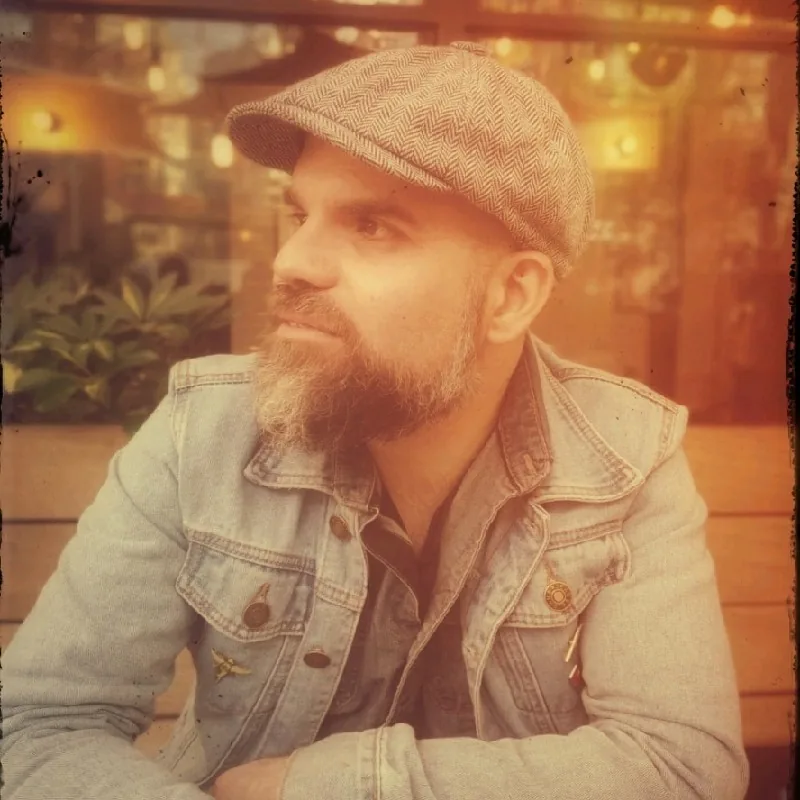 Portrait of Javier Riveros, strategic communicator, wearing a denim jacket and flat cap, looking to the side